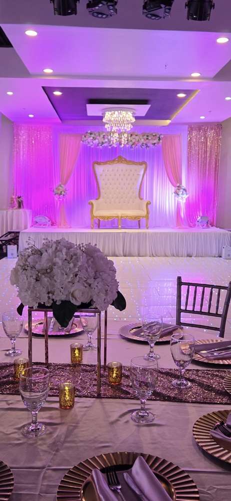 A tall white and gold throne chair on a blush draped stage under purple uplighting at Silverstar Event Center in Lewisville, TX