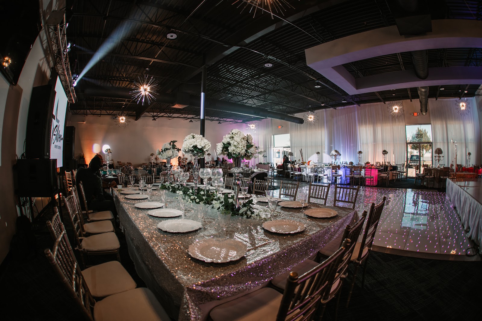 Wide fisheye view of the Silverstar Event Center hall dressed with a silver sequin head table, white florals and the LED dance floor at Silverstar Event Center in Lewisville, TX
