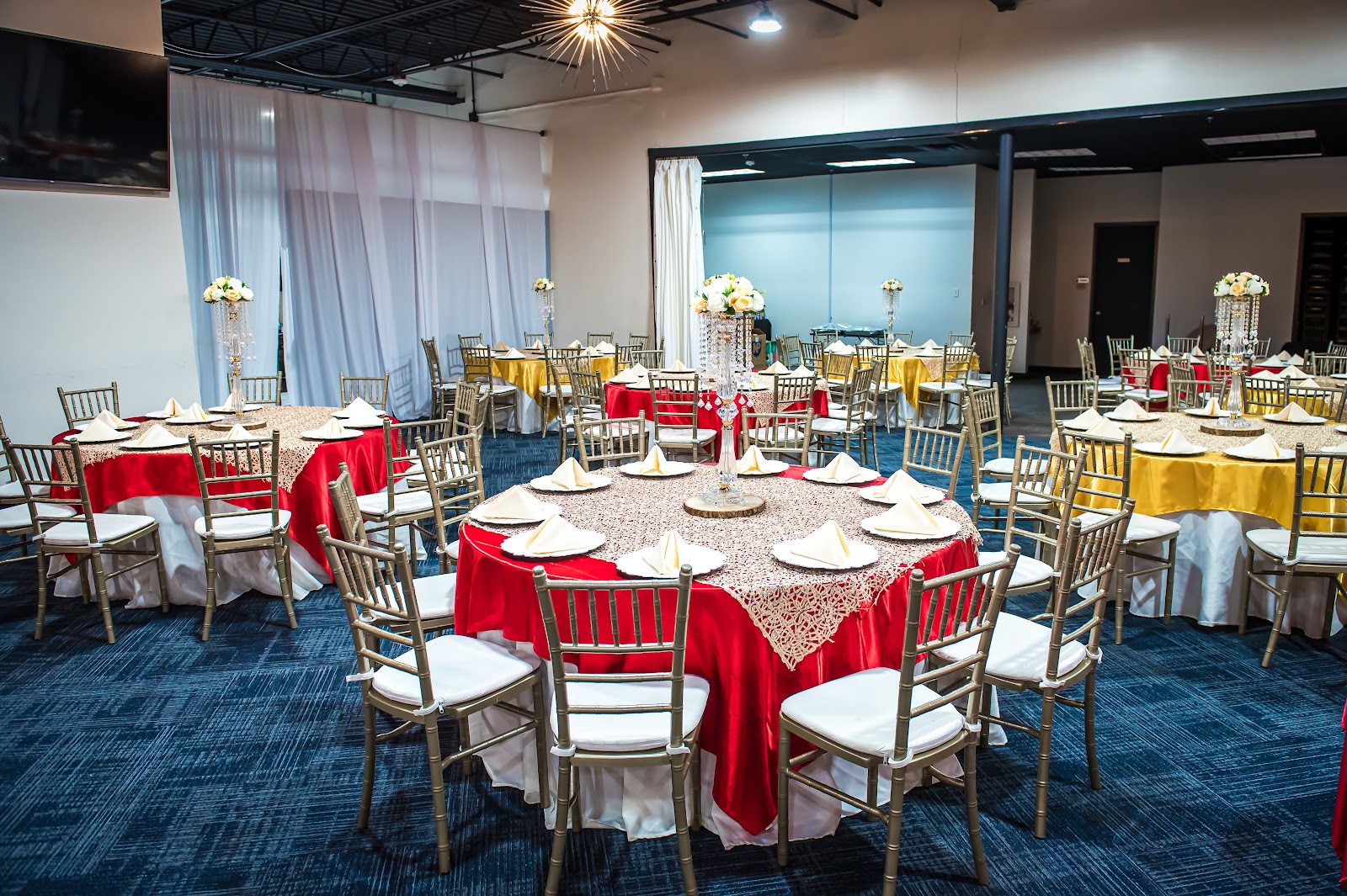 Round banquet tables dressed in red and gold linens with gold Chiavari chairs in the daytime hall at Silverstar Event Center in Lewisville, TX