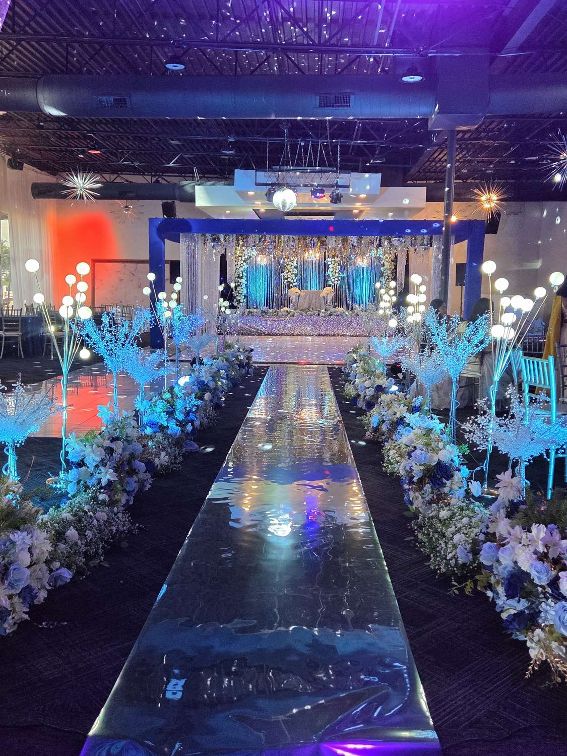 Mirrored aisle lined with lit florals leading to the stage at Silverstar Event Center in Lewisville, TX